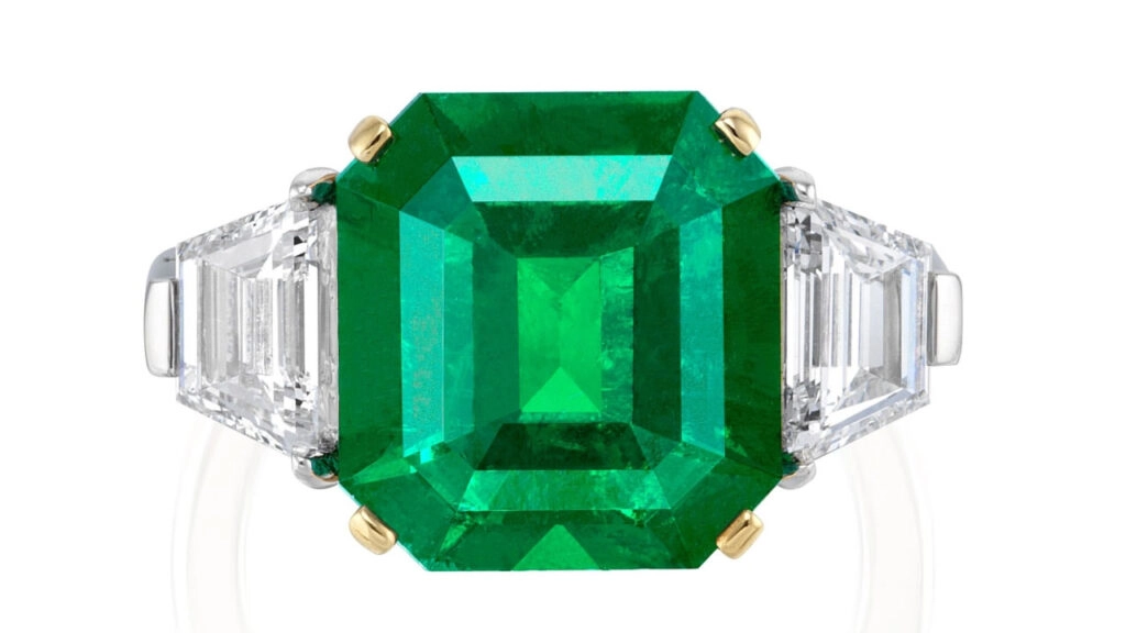 A step-cut, 5.89-carat, Colombian emerald is the star of this ring. The gemstone is flanked by two trapezoid step-cut diamonds at Phillips image