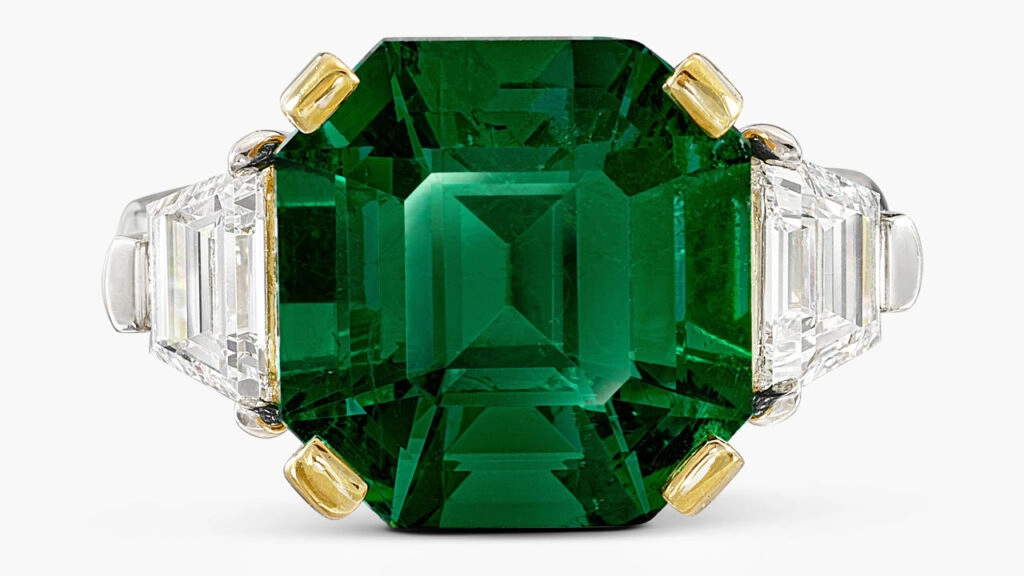 A ring with a step-cut, 7.90-carat Colombian emerald between two trapeze-shaped diamonds of 0.56 and 0.53 carats at Sotheby's image